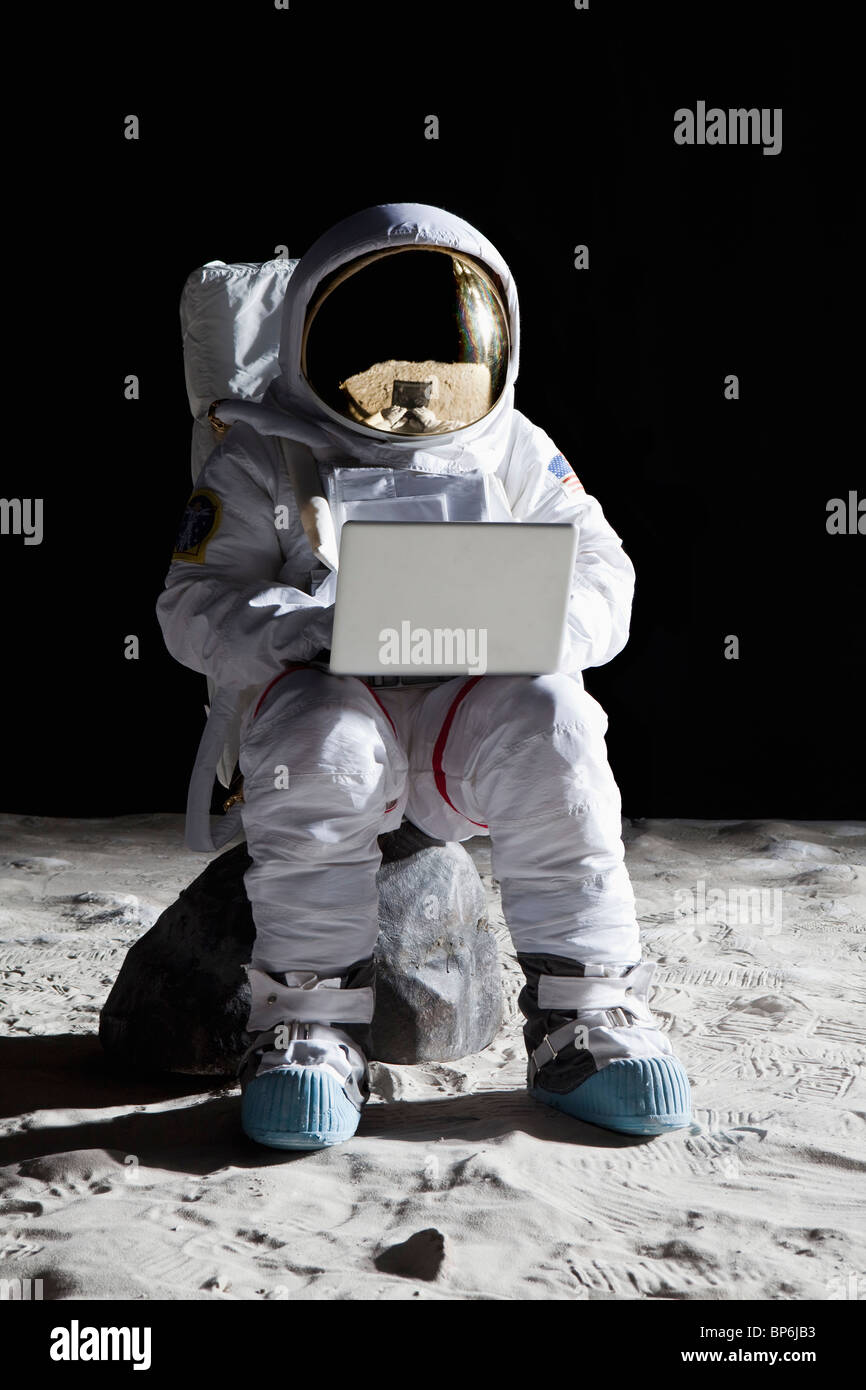 Ein Astronaut auf dem Mond sitzt auf einem Felsen mit einem laptop Stockfoto
