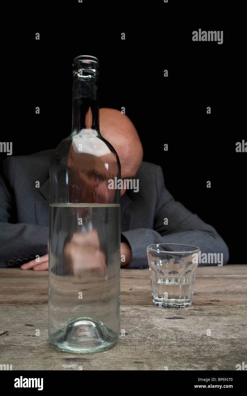 Betrunken und deprimiert Geschäftsmann mit einer Flasche Wodka und ein leeres Glas Stockfoto