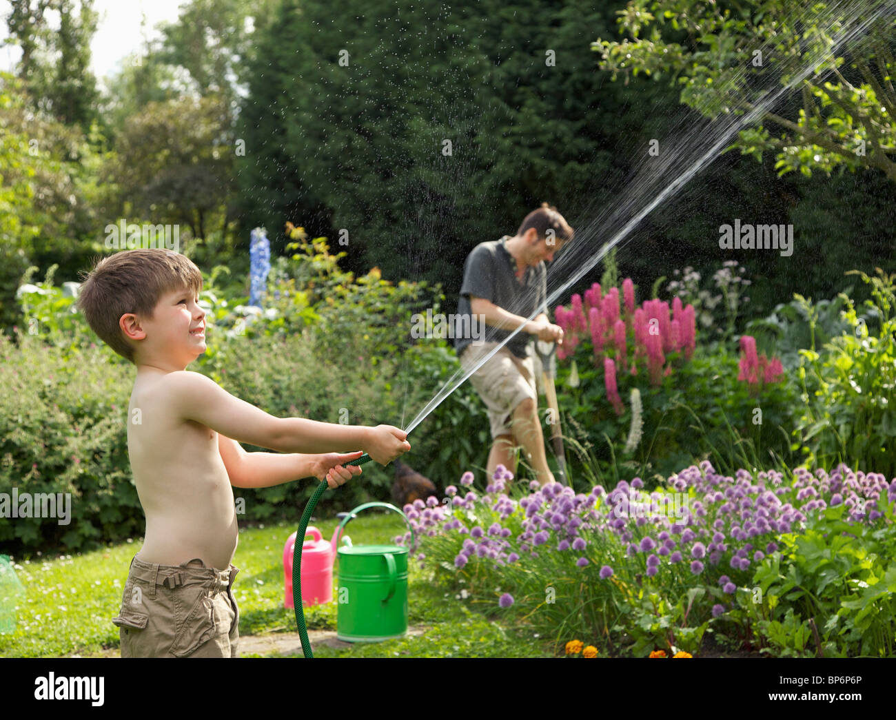 Ein Junge einen Schlauch in einen Garten Spritzen Stockfotografie