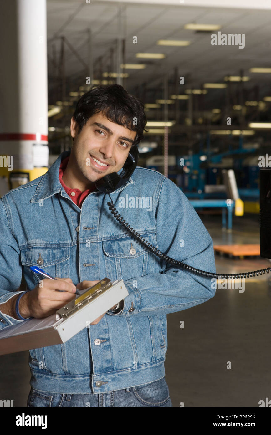 Fröhlicher Mensch mit Telefon in Fabrik Stockfoto