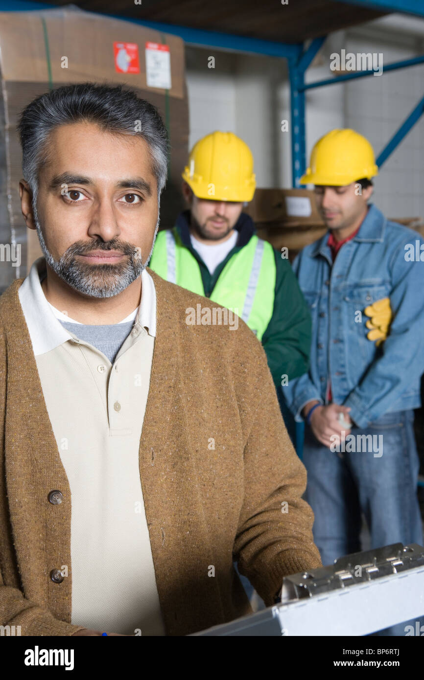 Ernste Männer in Fabrik, Kolleginnen und Kollegen im Hintergrund Stockfoto