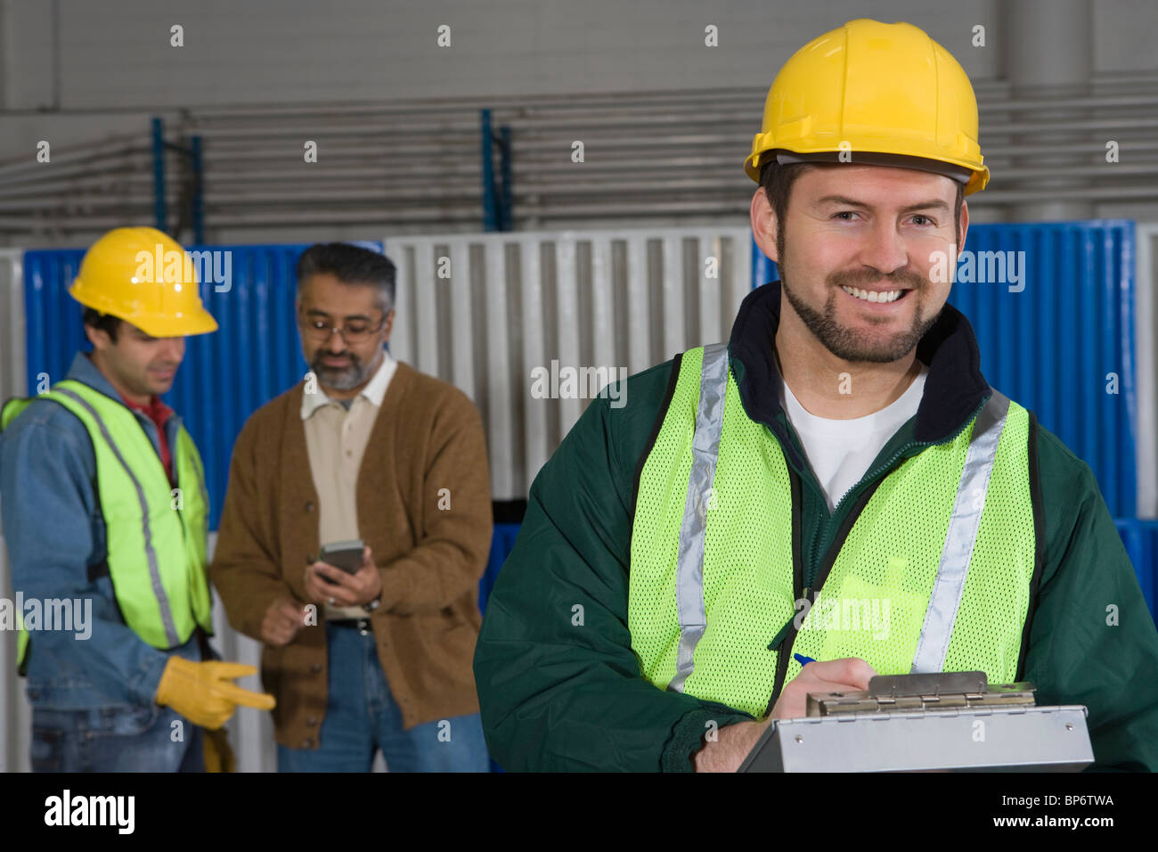Fröhlicher Mensch stehen in Fabrik, Kolleginnen und Kollegen im Hintergrund Stockfoto