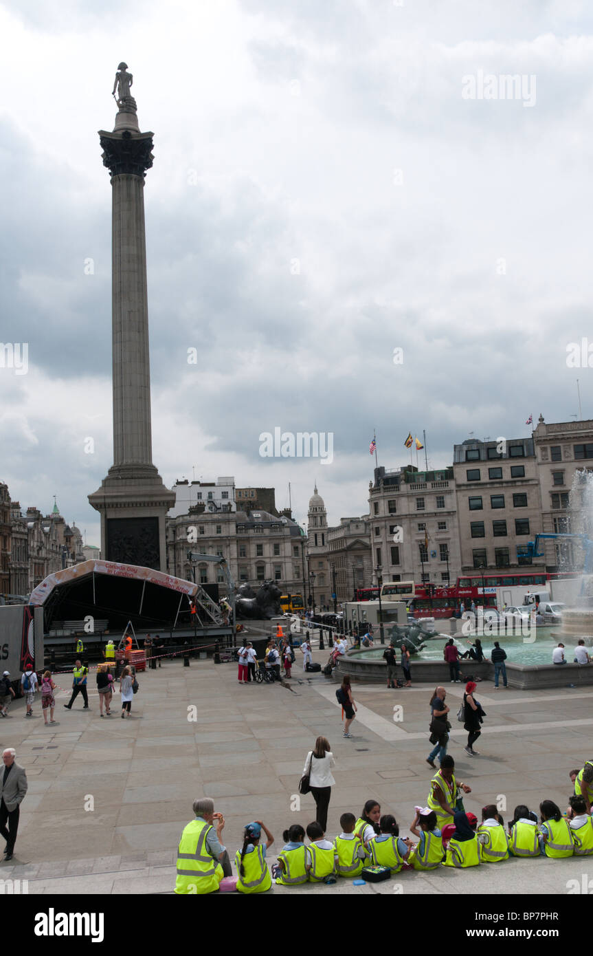 Eine Gruppe von Schulkindern auf einem Ausflug sitzen auf dem Trafalgar Square in London tragen High-Vis Jacken Stockfoto