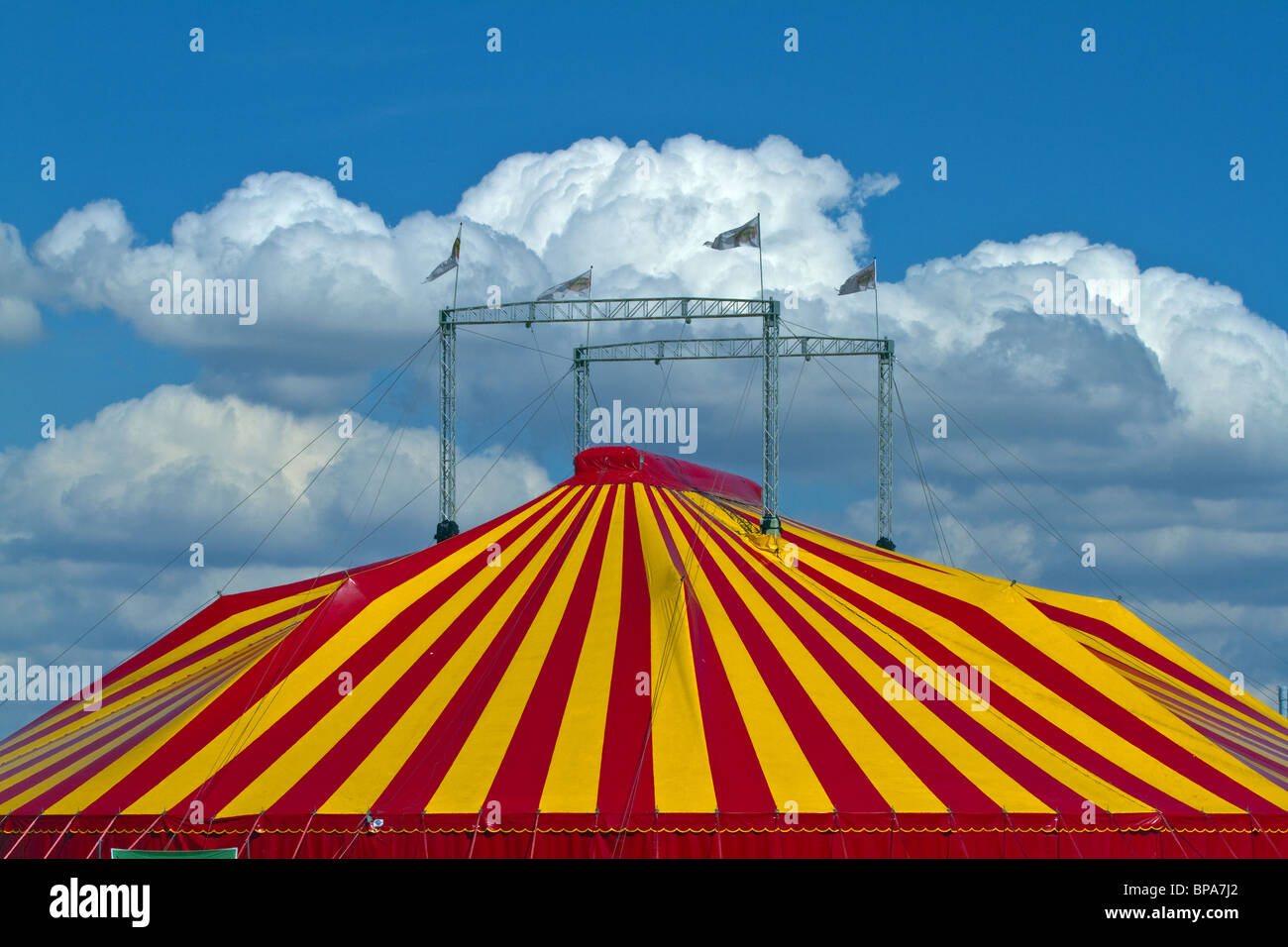Gestreifte Zirkuszelt vor blauem Himmel mit flauschigen Wolken. Horizontale Stockfoto
