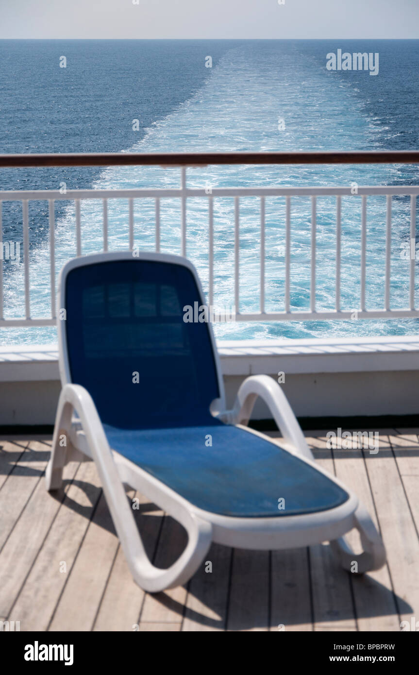 Eine blaue Sonnenliege am Heck eines Kreuzfahrtschiffes mit Gefolge im Hintergrund. Stockfoto