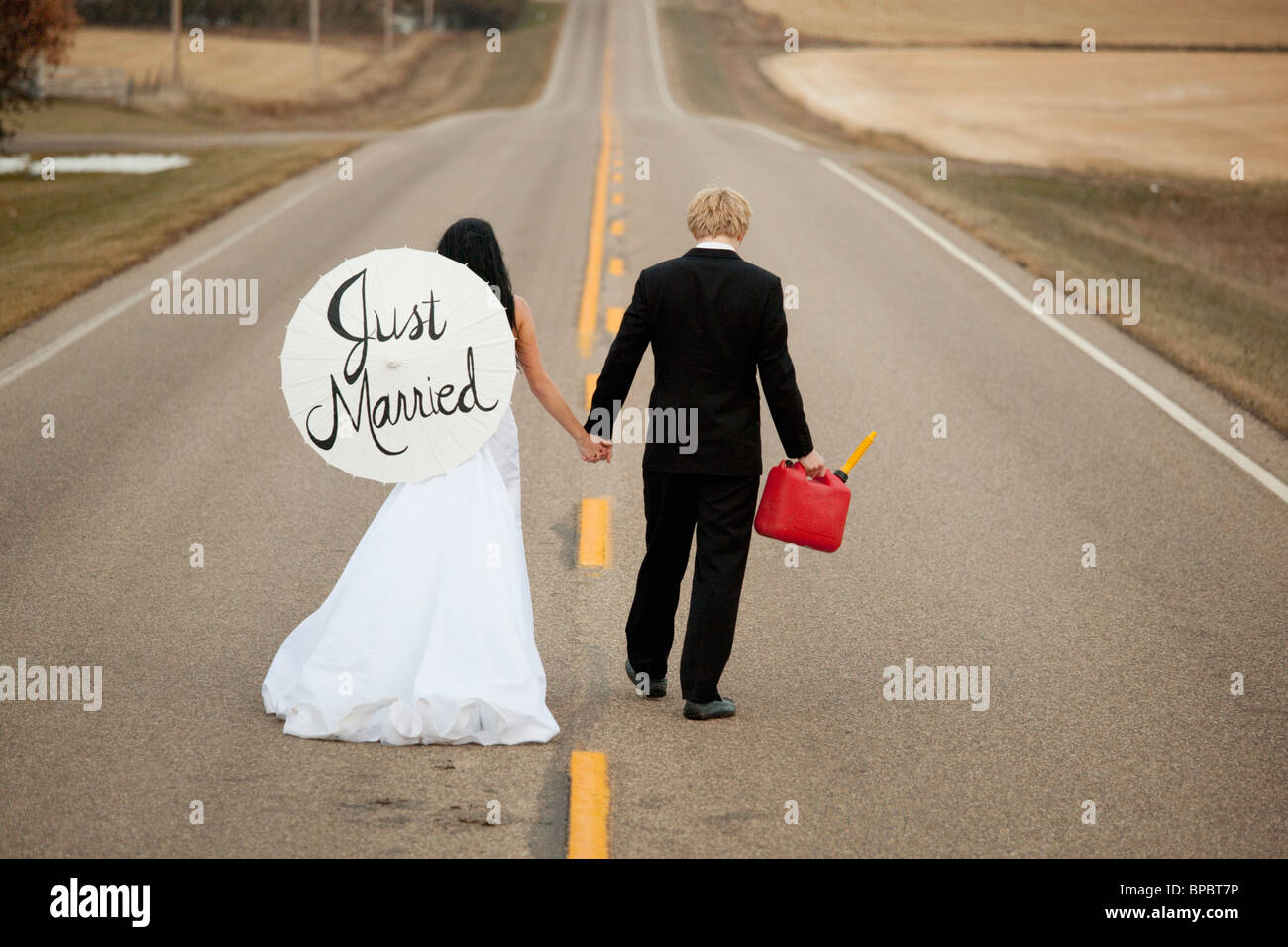 drei Hügel, Alberta, Kanada; eine Braut und Bräutigam zu Fuß auf einer Straße hält ein Kanister und ein Sonnenschirm, die sagen, "just married" Stockfoto