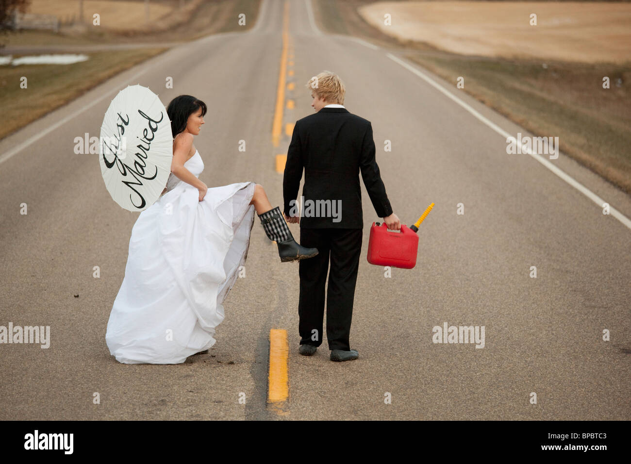 drei Hügel, Alberta, Kanada; spazieren auf einer ländlichen Straße mit einem Kanister und einem Sonnenschirm sagen "just married" Braut und Bräutigam Stockfoto
