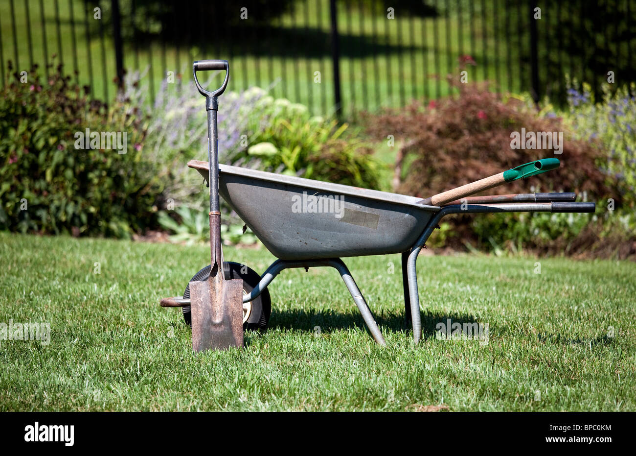 Garten Werkzeuge - Spaten Gleitstift gegen eine Schubkarre in einem Garten Stockfoto