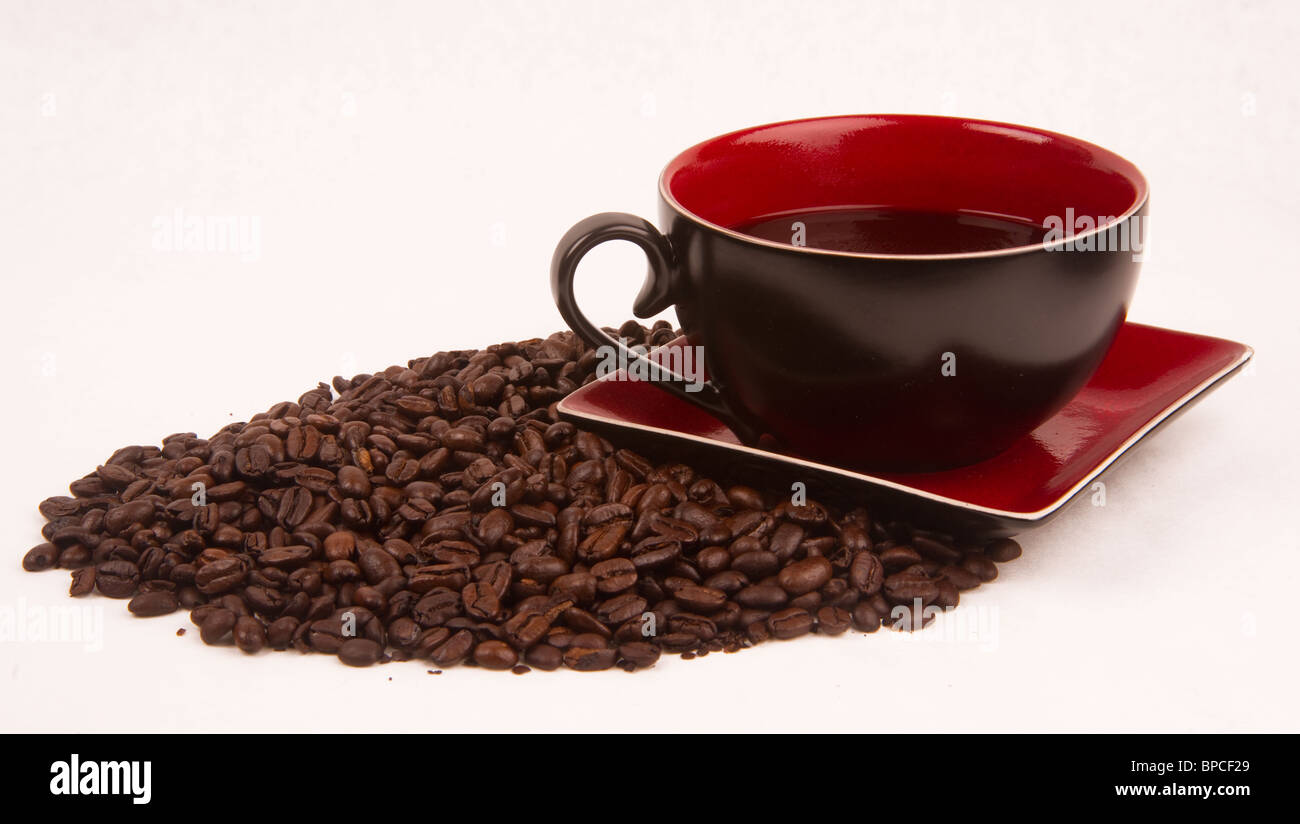 Eine Tasse Kaffee sitzen auf eine Untertasse auf einen Haufen von Kaffeebohnen. Stockfoto