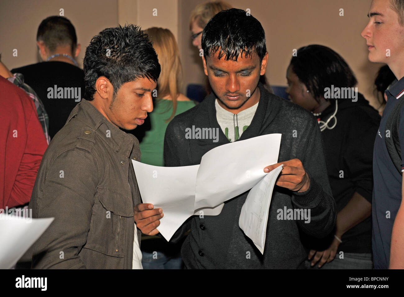 Eine junge männliche asiatische Studentin vorläufig betrachtet seine Prüfung Papiere mit einem Freund auf Stockfoto