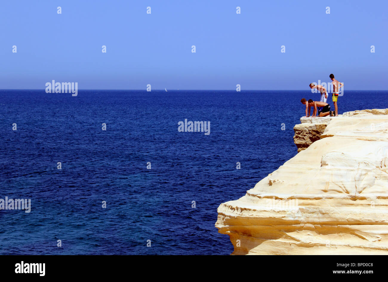 Vier jungen oder junge Männer am Rand einer Klippe über dem Meer auf der Suche nach unten; bei El Playazo, südlich von Las Negras, Cabo de Gata-Spanien Stockfoto