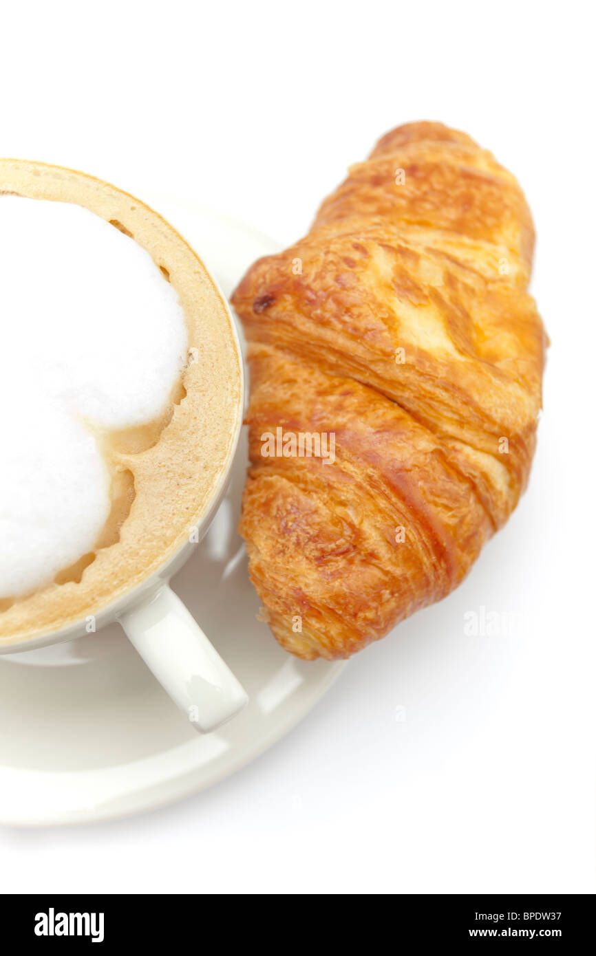 Frisch gebackenes Croissant neben einer Tasse Cappuccino auf weißem Hintergrund. Stockfoto