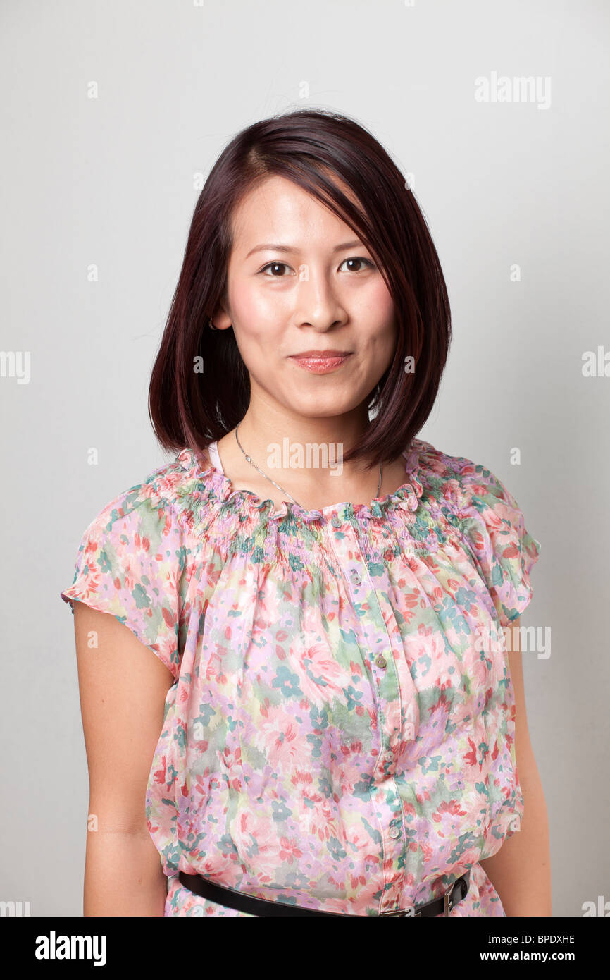 Porträt einer lächelnden jungen asiatischen Frau in einer Blumenbluse vor neutralem Hintergrund. Stockfoto