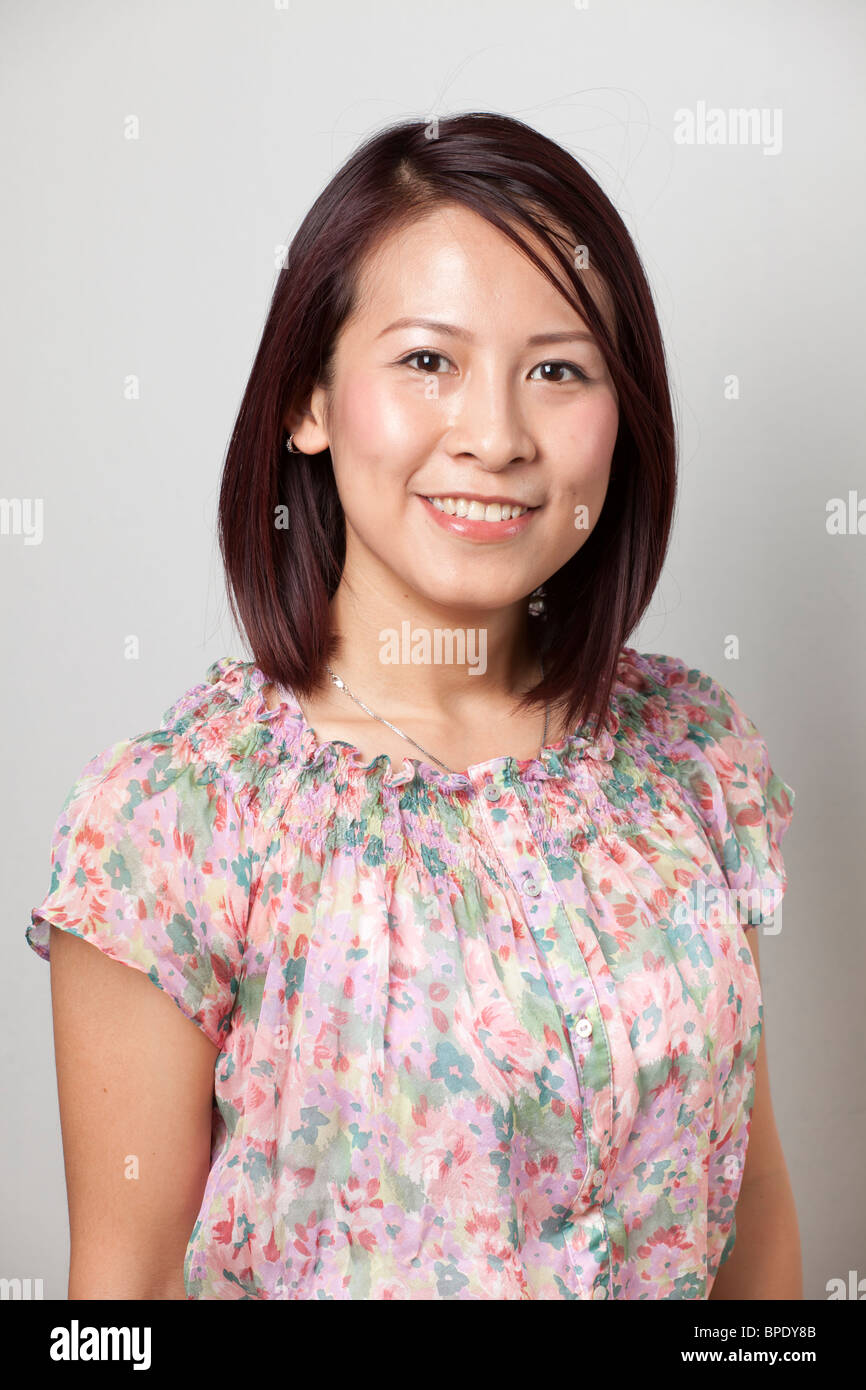 Porträt einer lächelnden jungen asiatischen Frau in einer Blumenbluse vor neutralem Hintergrund. Stockfoto