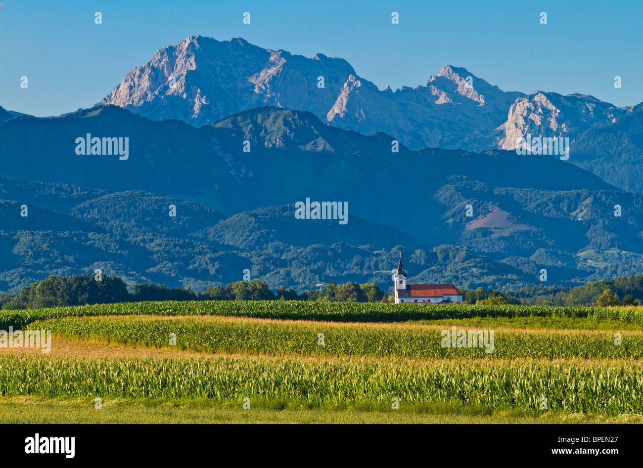 Die Steiner Alpen erhebt sich hinter einer Kirche in der Region Gorenjska Sloweniens. Stockfoto