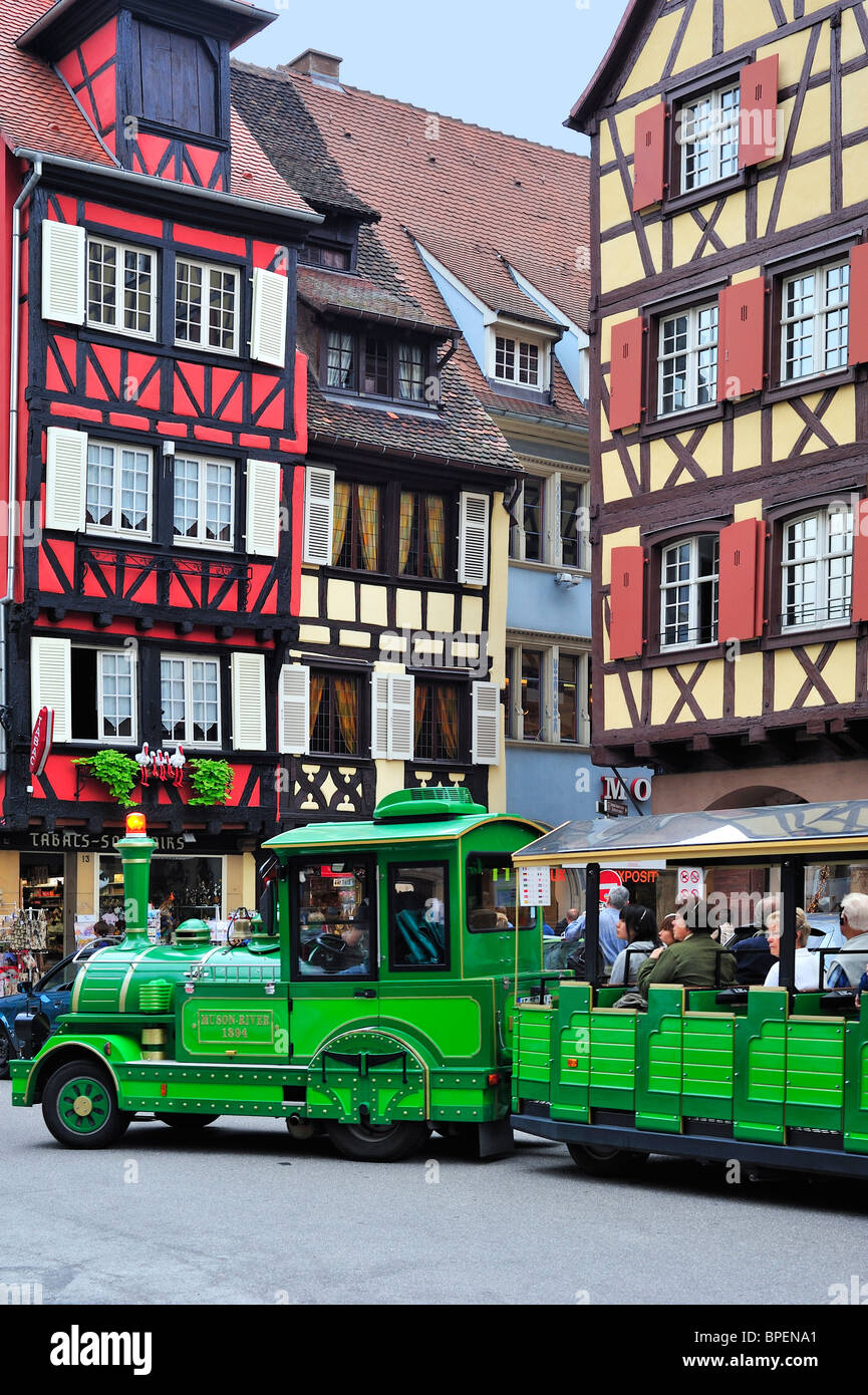 Bunte Fassaden umrahmt Holzhäuser und Sightseeing-Zug mit Touristen in Colmar, Elsass, Frankreich Stockfoto