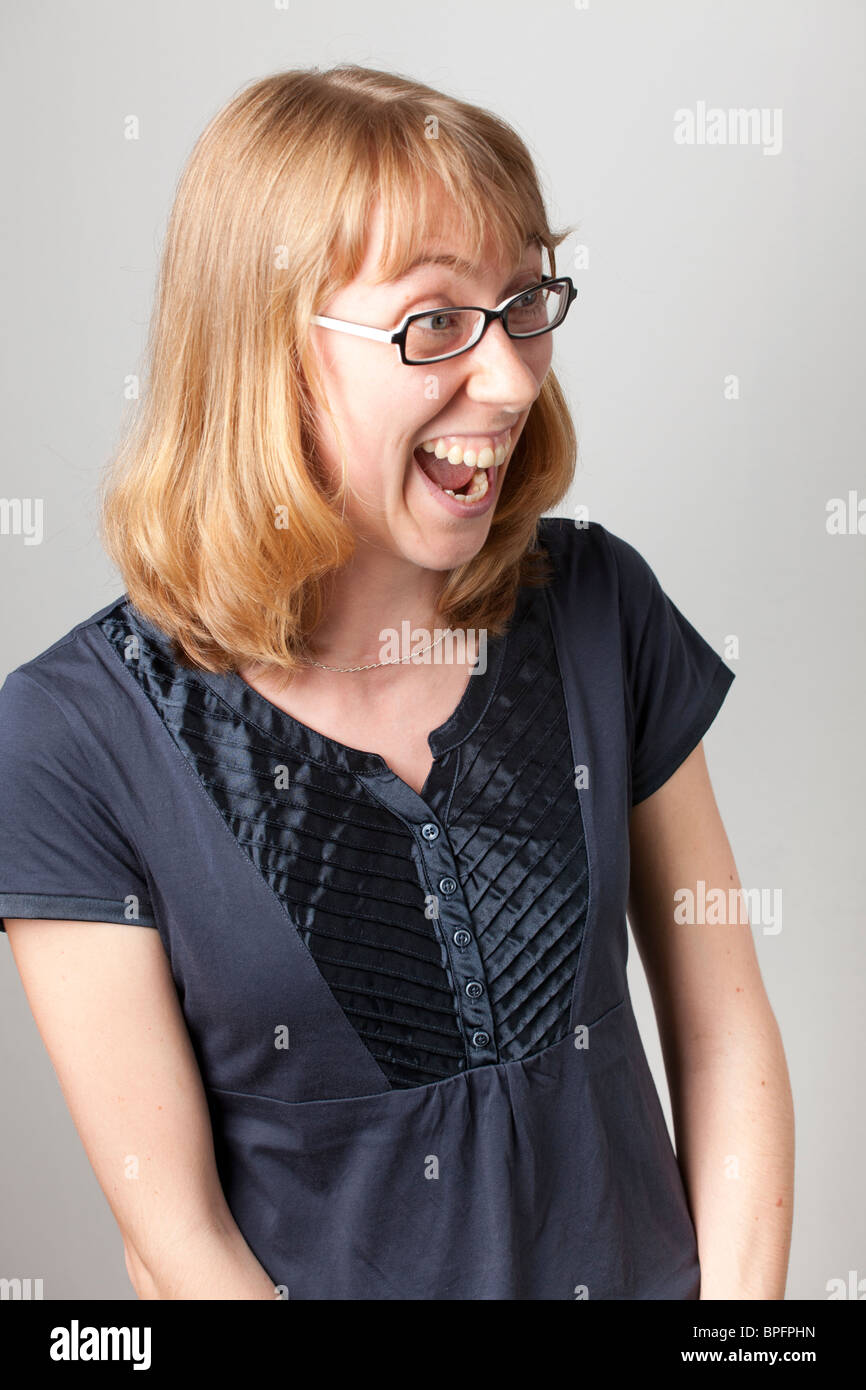 Aufgeregte Frau mit blonden Haaren und Brille, die lacht und zur Seite schaut, trägt ein dunkelblaues Oberteil, in einem ehrlichen Moment festgehalten. Stockfoto
