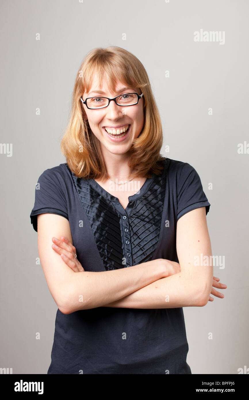 Lächelnde Frau mit Brille, überkreuzte Arme, eine dunkelblaue Bluse, die direkt in die Kamera blickt. Stockfoto