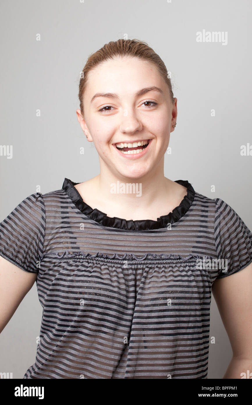 Lächelnde junge Frau in einer gestreiften Bluse mit kurzen Ärmeln, die vor einem schlichten Hintergrund direkt in die Kamera blickt. Stockfoto