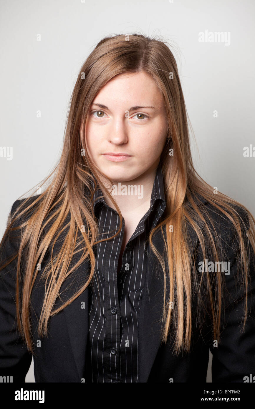 Ernsthafte junge Frau in schwarzem Blazer und gestreiftem Hemd, mit langen glatten Haaren, die direkt in die Kamera blickt. Stockfoto