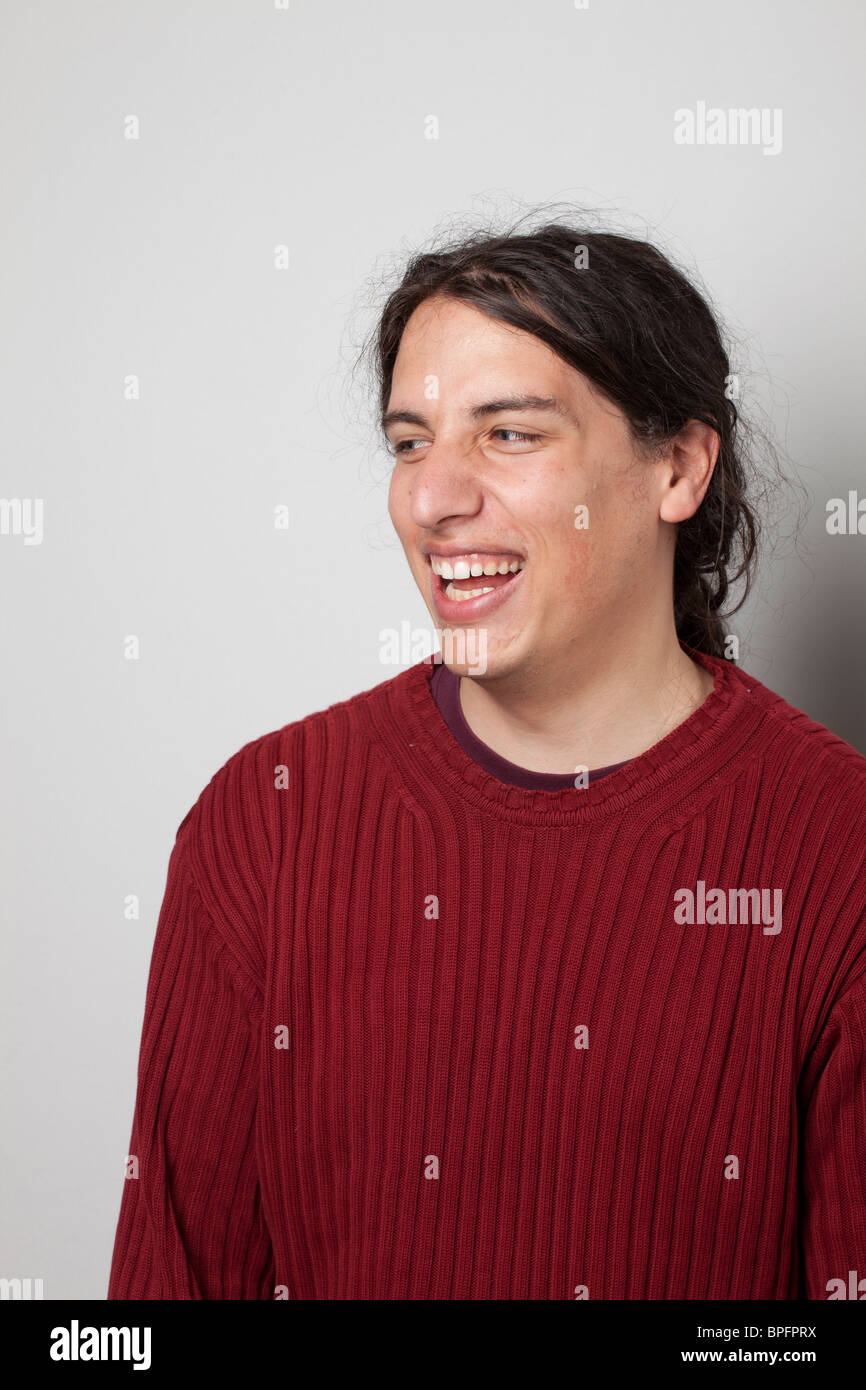Junger Mann in einem roten Pullover lächelt und schaut zur Seite vor einem neutralen Hintergrund. Stockfoto