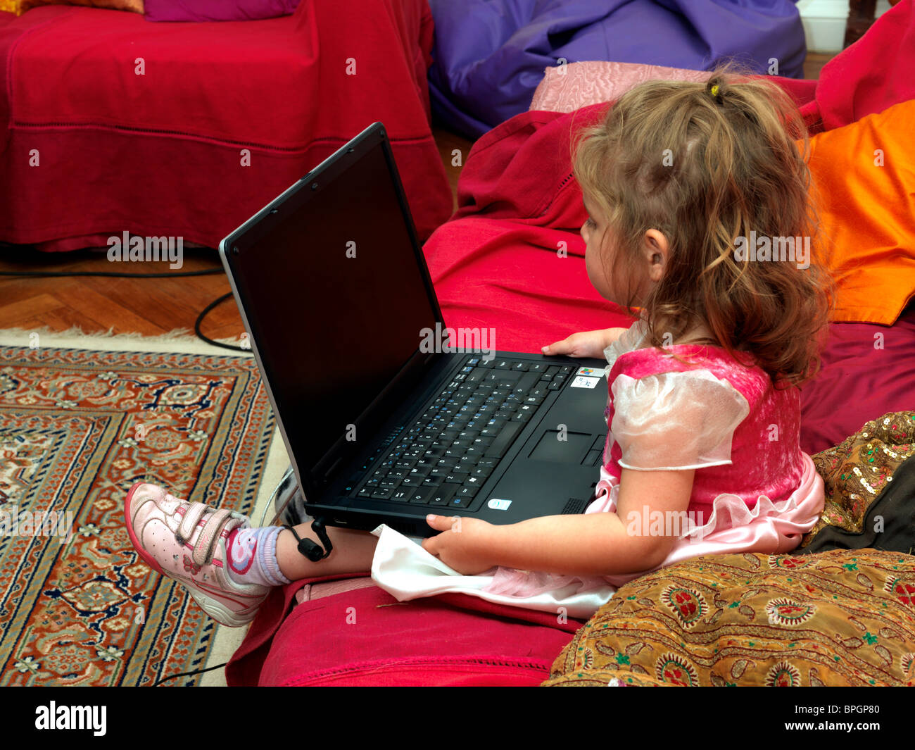 3-jähriges Mädchen auf Sofa Blick auf Laptop Stockfoto