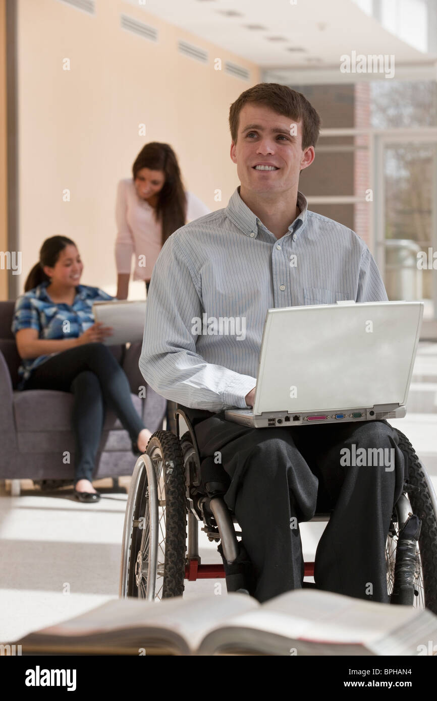 Lehrer mit Querschnittslähmung im Rollstuhl mit ihren Schülern im Hintergrund Stockfoto