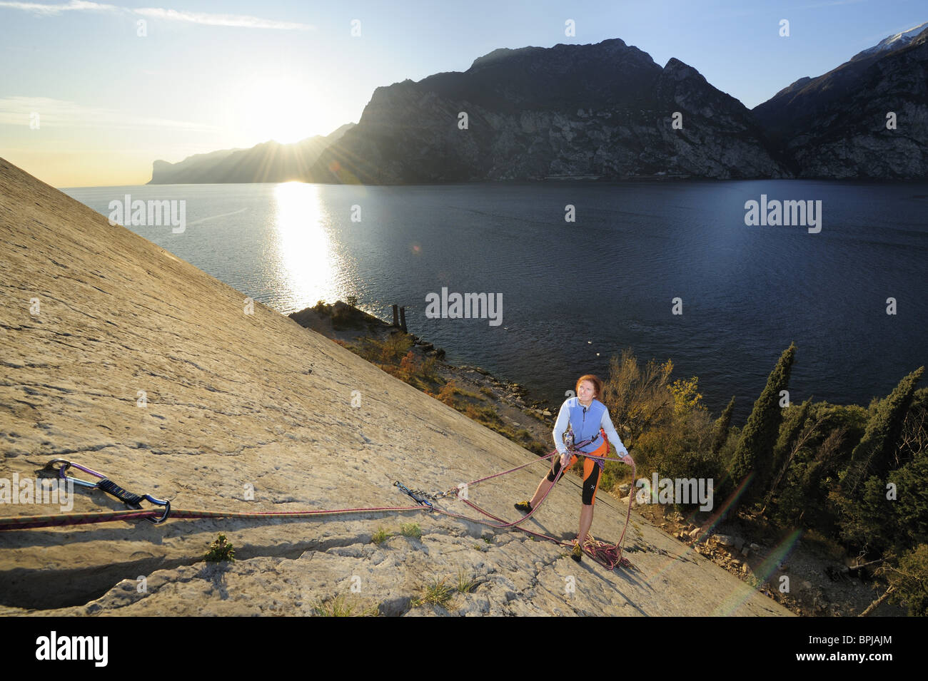 Frau Klettern am Felsvorsprung Corno di Bo, Gardasee im Hintergrund, Nago-Torbole, Trentino-Alto Adige/Südtirol, Italien Stockfoto