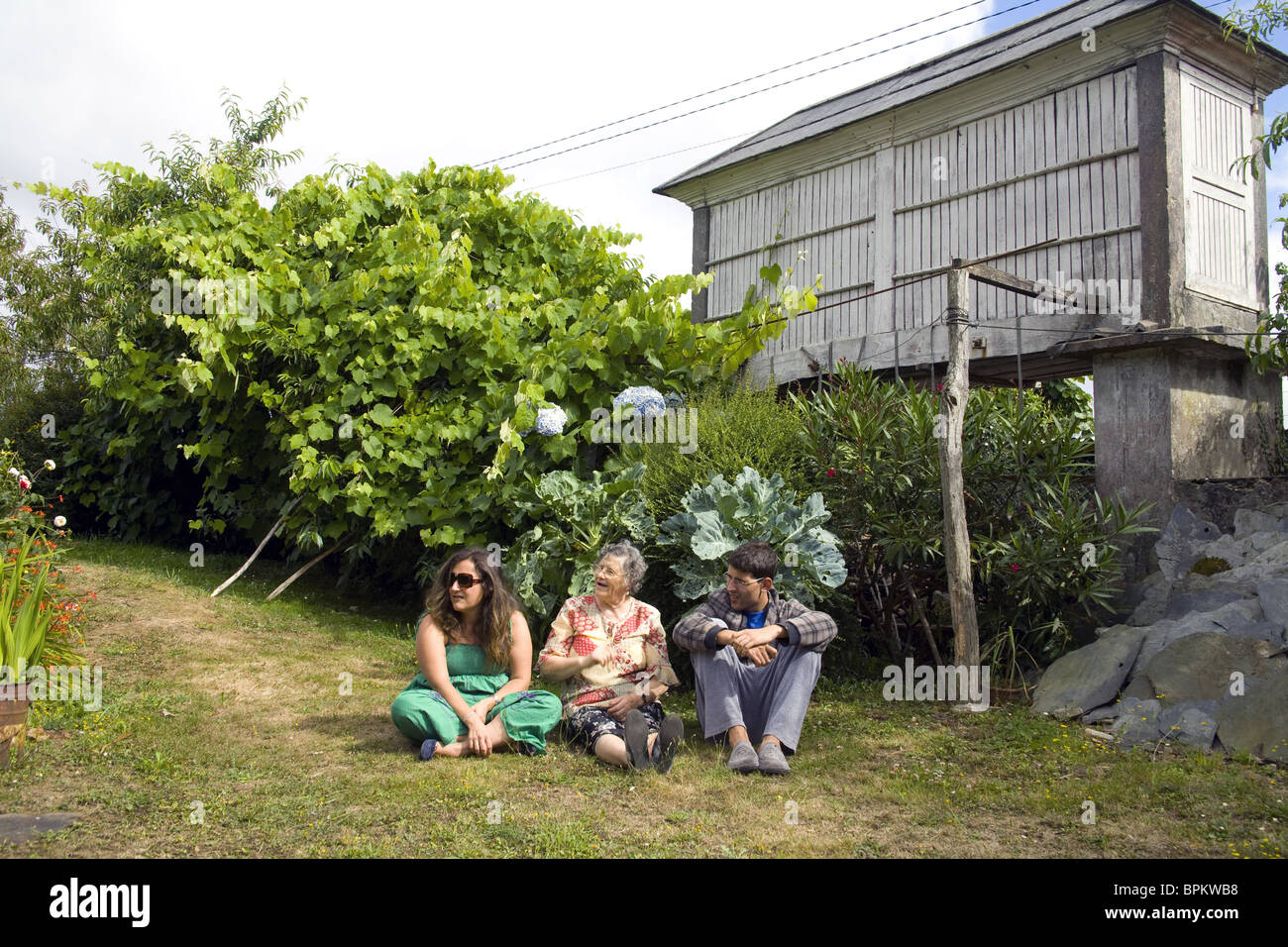 Drei Personen sitzen entspannt im Hinterhof eines traditionellen galizischen Landhauses Stockfoto