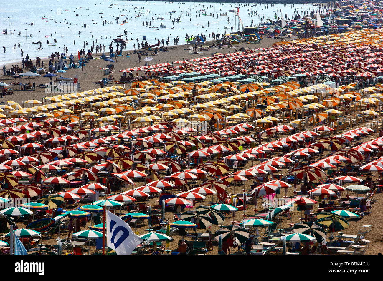 Massentourismus am Strand von Caorle, Adria, Italien. Tausende von Sonnenliegen und Sonnenschirme, Sonnenschirme. Stockfoto