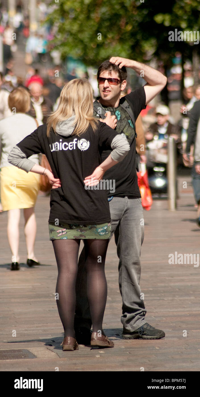 Ein weiblicher Liebe Arbeiter hält einen Mann in einer Glasgow-Straße um ihn für eine monatliche Spende Lastschriftverfahren anmelden. Stockfoto