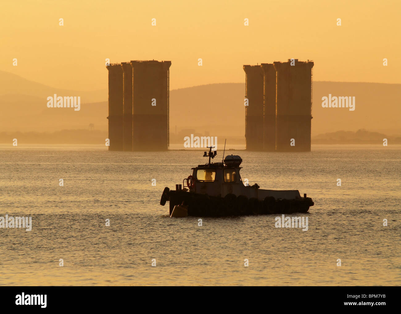 Ein Workboat liegt neben den Beinen einer Nordsee-Öl-Plattform wie die Sonne über den Cromarty Firth, Schottland. Stockfoto