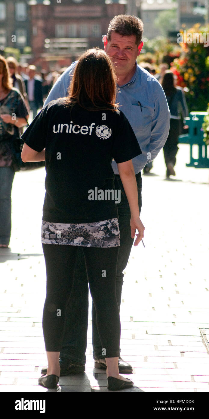 Ein weiblicher Liebe Arbeiter hält einen Mann in einer Glasgow-Straße um ihn für eine monatliche Spende Lastschriftverfahren anmelden. Stockfoto