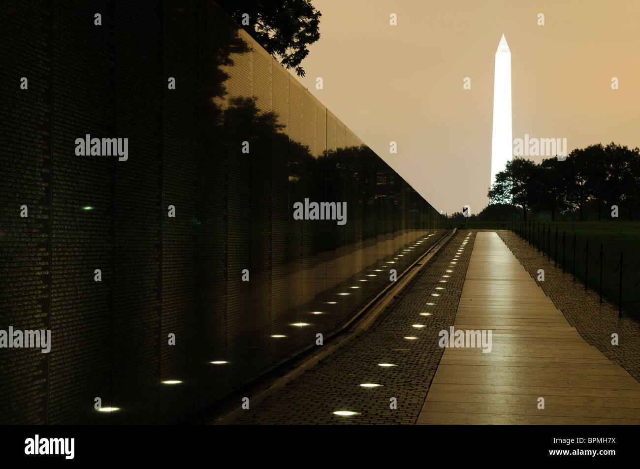 WASHINGTON DC, USA - Night Shot des Vietnam Veterans Memorial mit dem Washington Monument mit dem orangen Schein der Lichter der Stadt gegen niedrige Wolken. Stockfoto