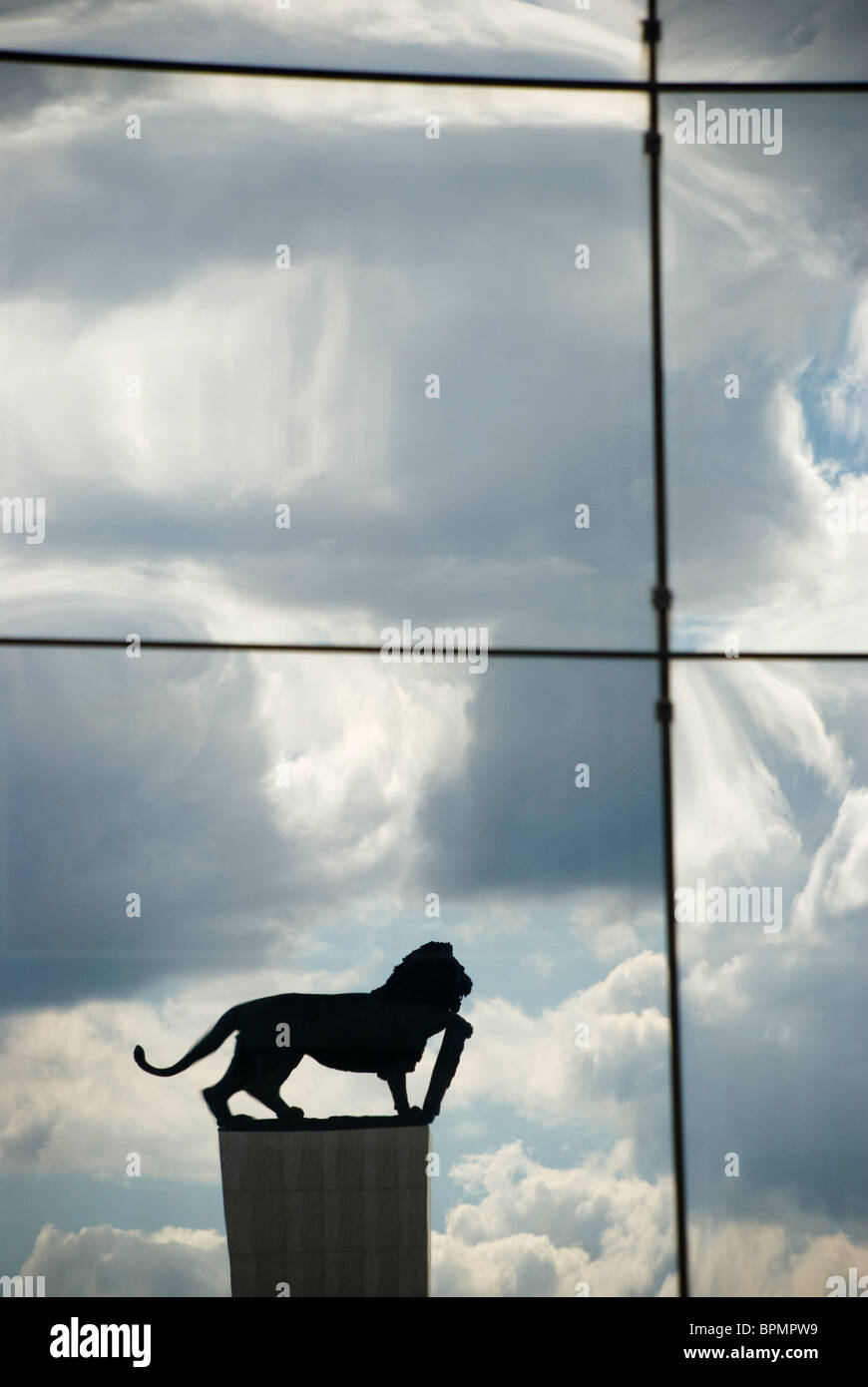 Wolken reflektiert auf die Glaswand mit Statue des Löwen Stockfoto