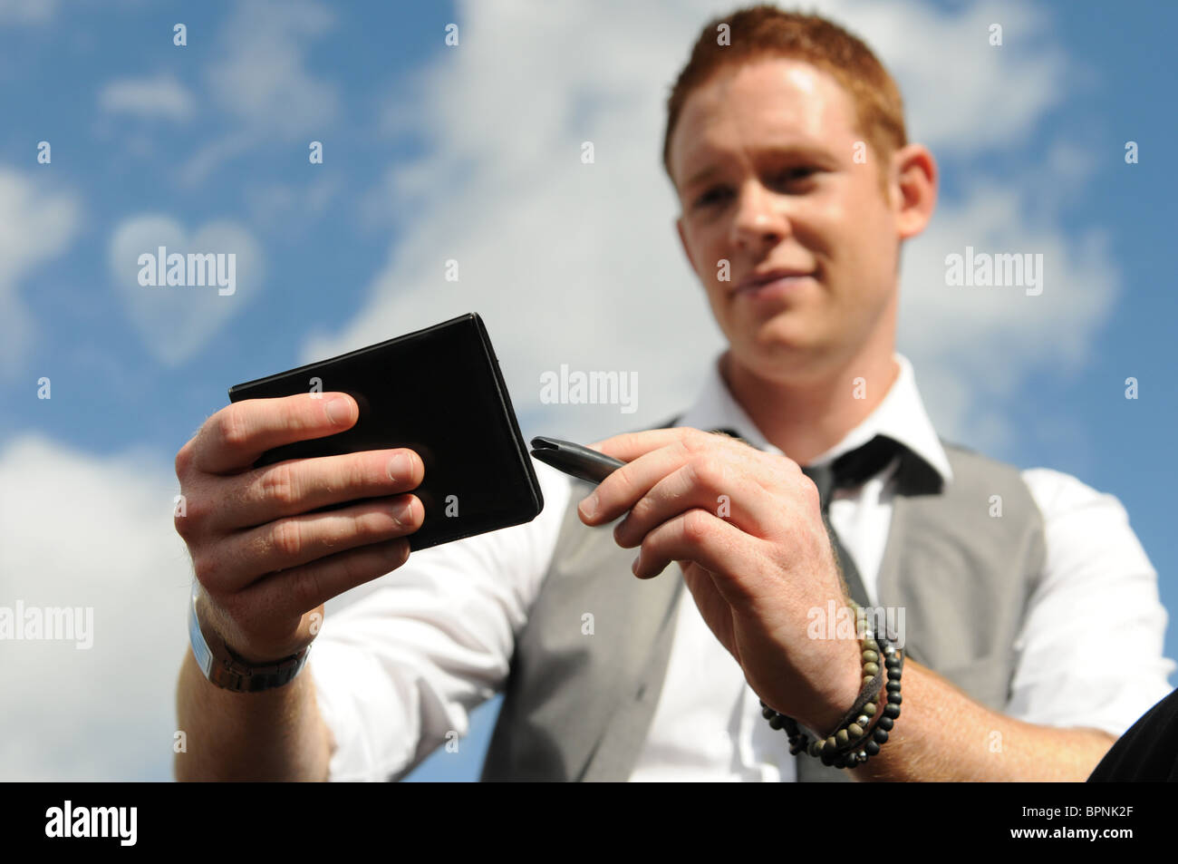 junger weißer Mann mit Ingwer Haar sitzt draußen mit Notizblock und Stift einen Liebesbrief schreiben Stockfoto