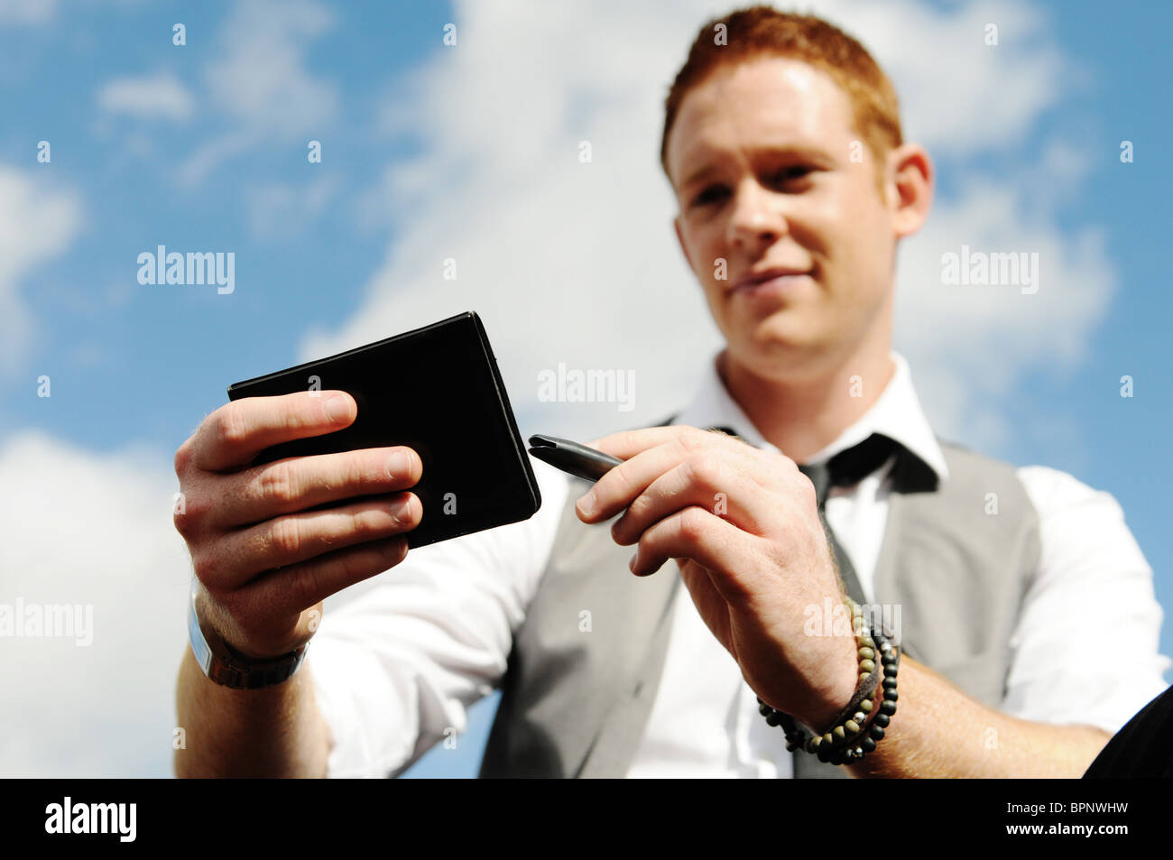junger weißer Mann mit Ingwer Haar Sitz außerhalb mit Notizblock und Stift schreiben Stockfoto