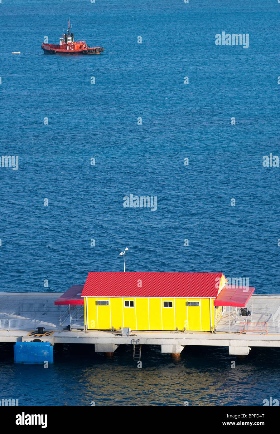 Eine rote und gelbe Gebäude auf einer Mole mit einem roten Schlepper auf dem blauen Wasser Stockfoto
