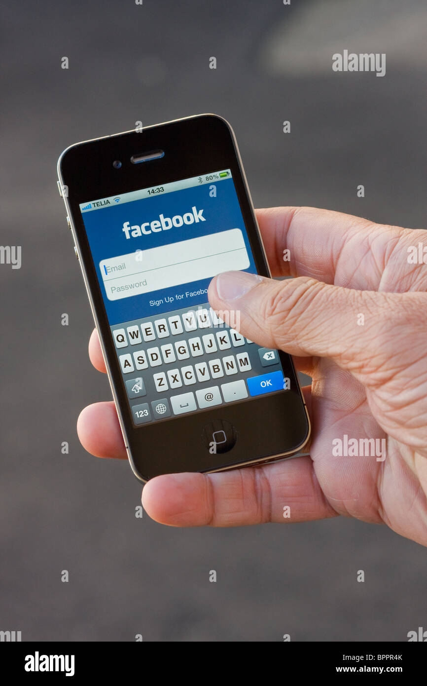 Das iPhone 4 in der Handfläche der Hand eines Mannes. Auf dem Bildschirm sehen Sie die Facebook-app. Stockfoto