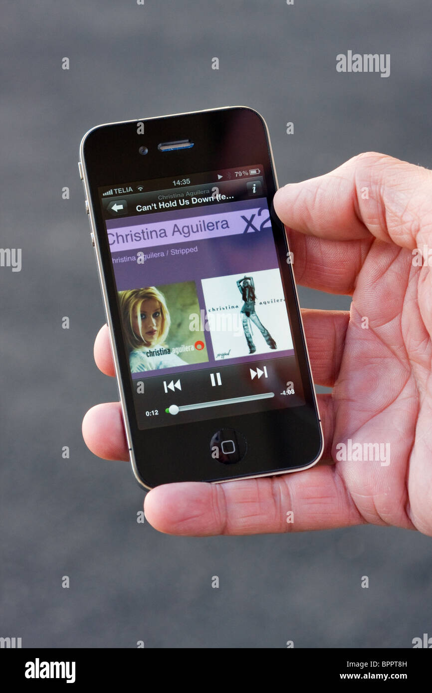 Das iPhone 4 in der Handfläche der Hand eines Mannes. Auf dem Bildschirm sehen Sie die Spotify app mit Christina Aguilera spielen. Stockfoto