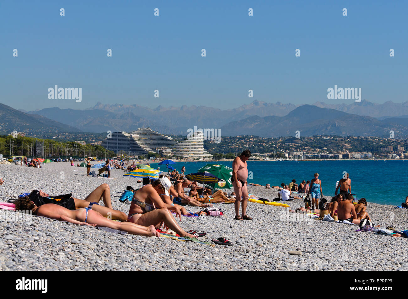 Menschenmassen am Kiesstrand in Antibes und Villeneuve Loubet, mit Blick auf Nizza. Stockfoto