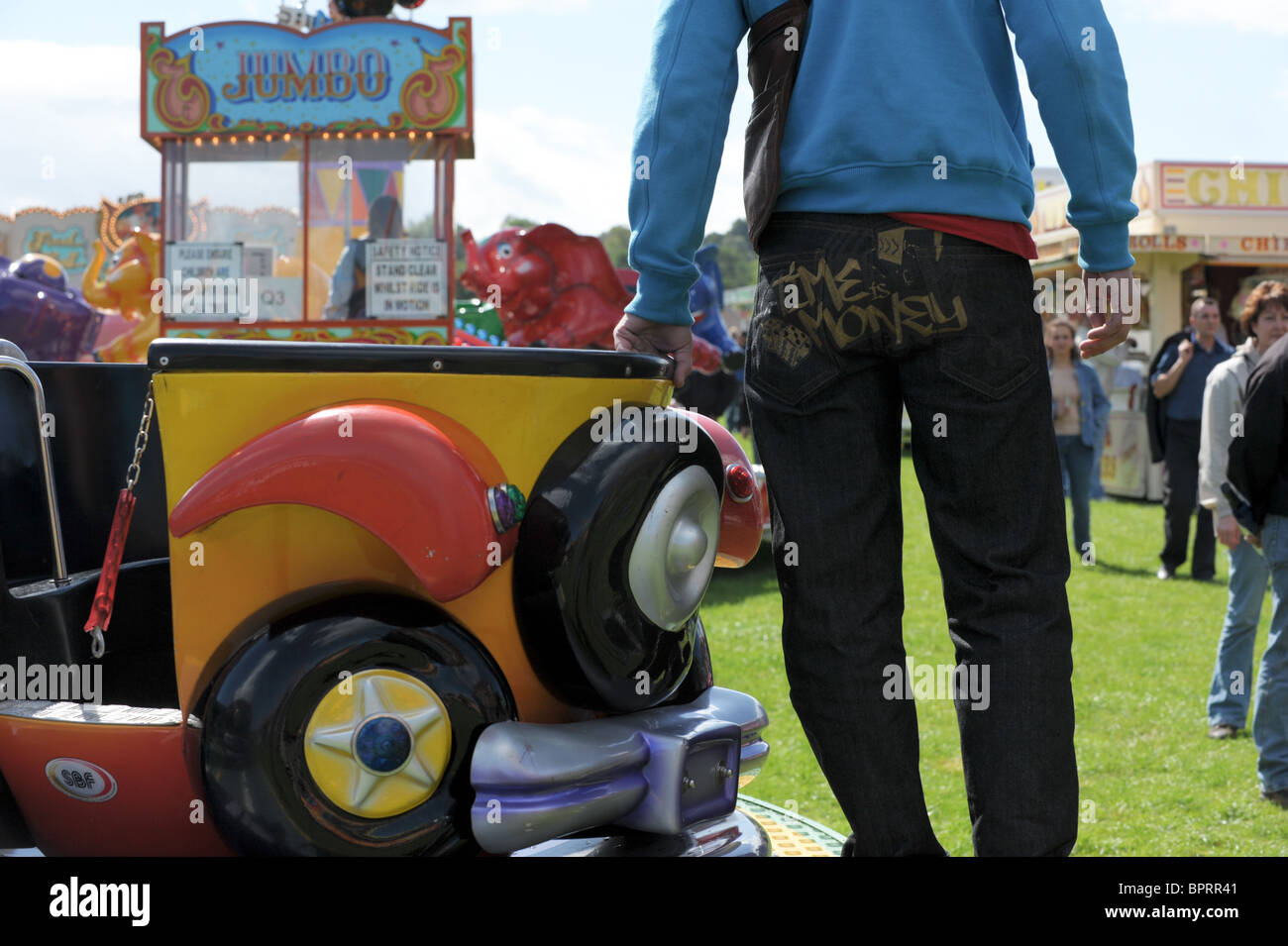 Messe-Arbeiter stehend auf einem leeren Kinder Fahrt mit der Zeit ist Geld, geschrieben auf der hinteren Tasche seiner Jeans Stockfoto