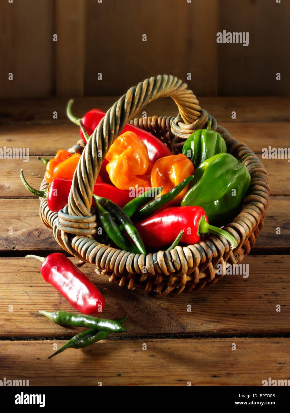 Gemischte frische chiilies (Chili) in einem Korb gegen eine Holz Hintergrund Stockfoto