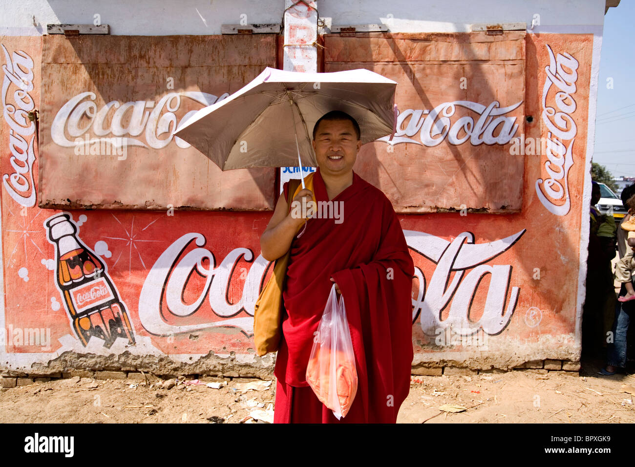 Porträt eines tibetisch-buddhistischen Mönchs gegen eine Wand sponsoring Coca Cola, Bodhgaya, Bihar, Indien. Stockfoto