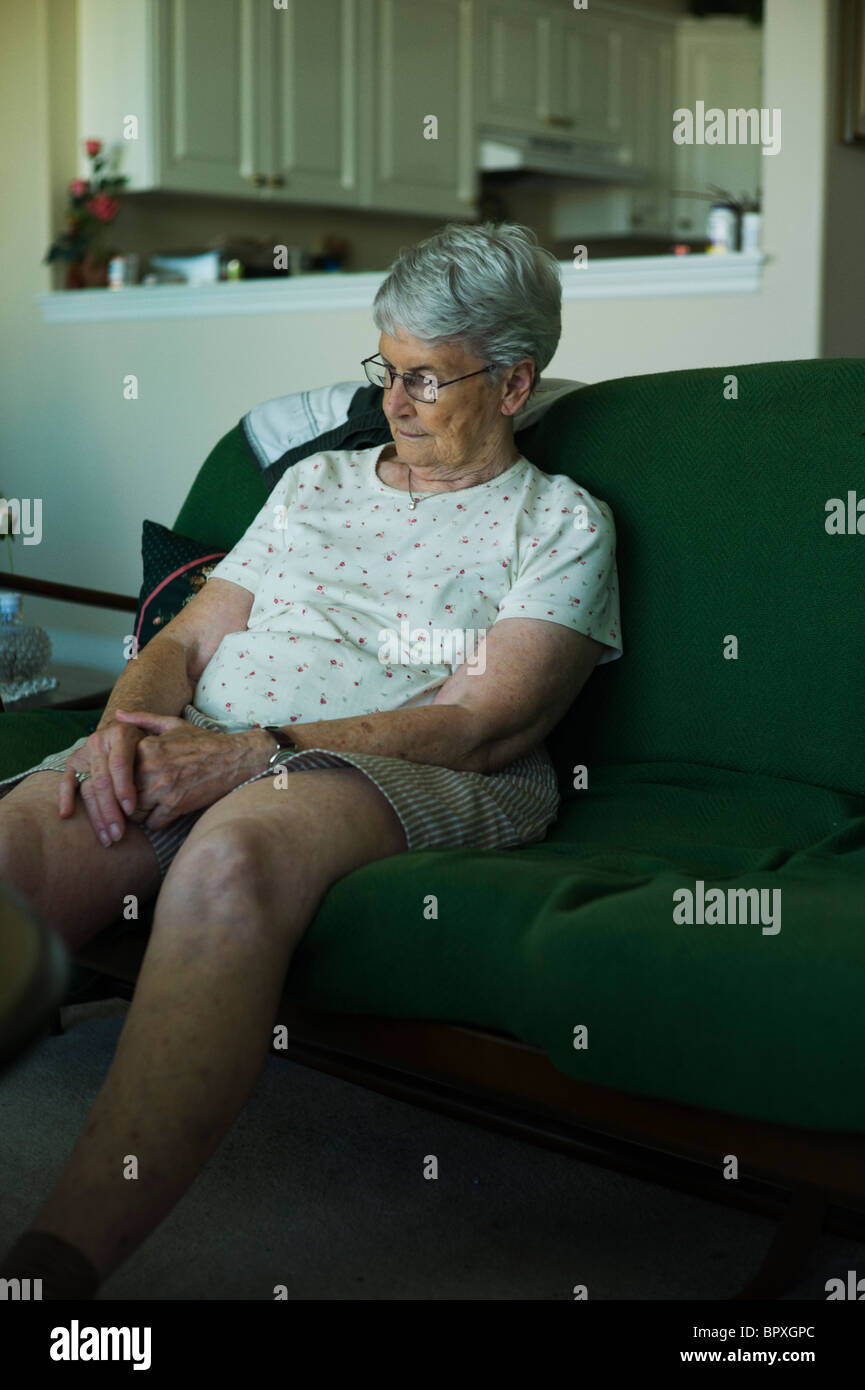 Sad aussehende Frau sitzen auf Wohnzimmer Couch mit Hände in den Schoß. Stockfoto