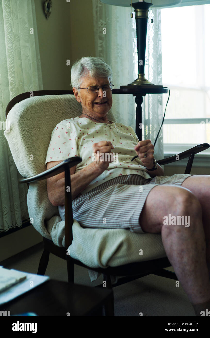 Alte Frau sitzt mit geballten Fäusten in Wohnzimmersessel Stockfoto