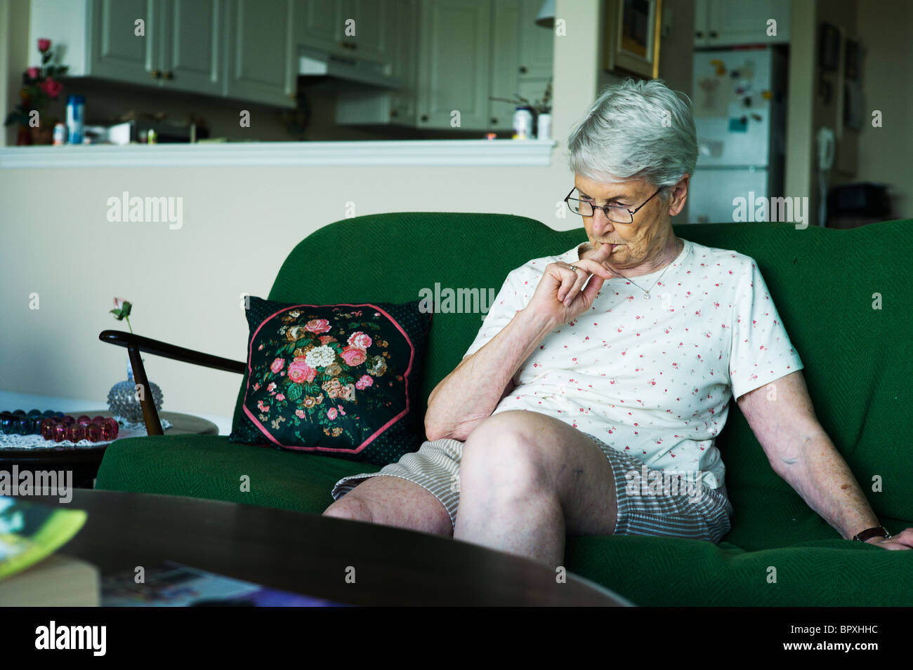 Alte Frau sitzt auf der Couch im Wohnzimmer kaut Fingernägel. Stockfoto