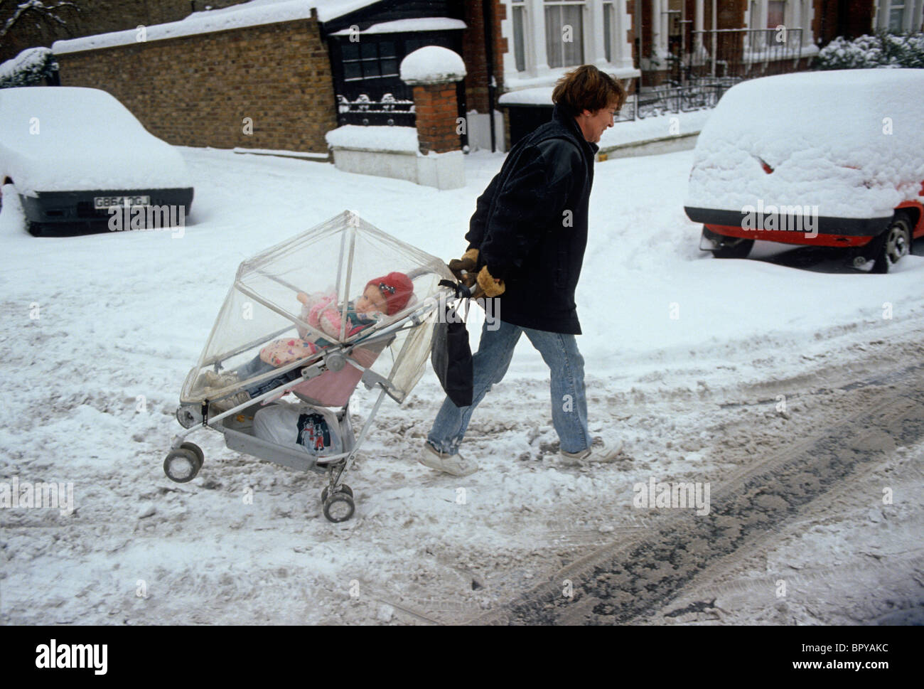 Eine Mutter kämpft um ihr Kind über frisch gefallenem Schnee in einer Londoner Straße ziehen. Stockfoto