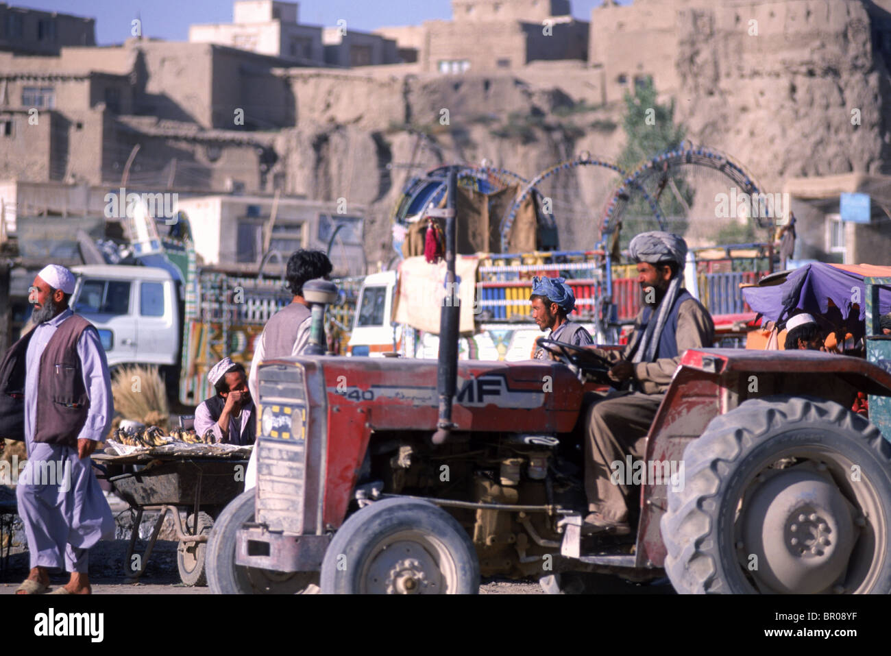 Ein Traktor fährt durch einen belebten Markt, der unter der alten Stadtmauer in der Stadt Ghazni, Afghanistan blüht. Stockfoto