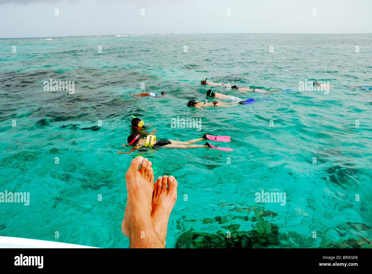 Belize, bleiben Füße über die Seite eines Bootes.  Schnorchler im Hintergrund. Stockfoto
